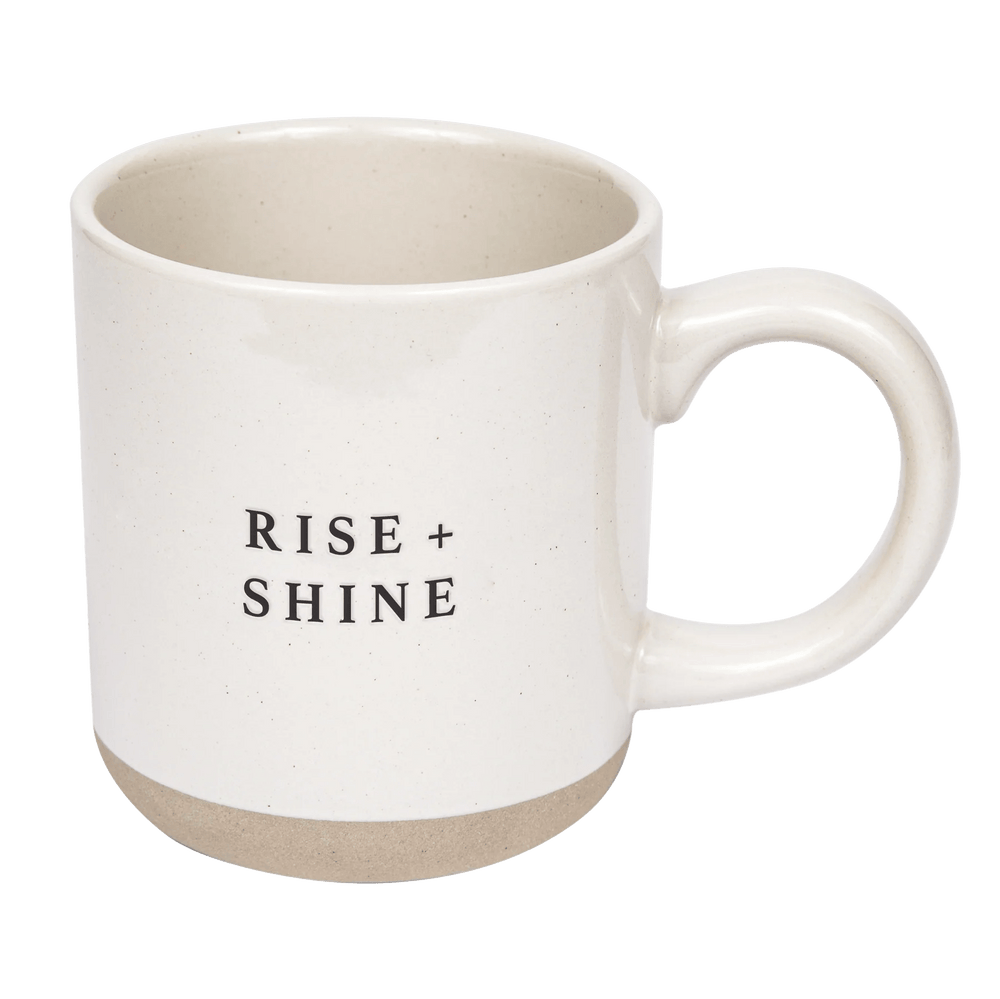 Cream colored coffee or tea cup with inscription Rise and Shine by Sweet Water Decor against white background.