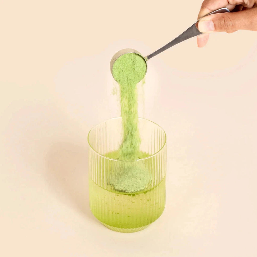 Dosierlöffel gibt Matcha Kollagen Lemon Flavour Pulver in Glas mit Flüssigkeit. North Glow