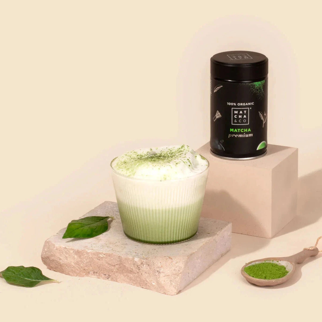 MATCHA & CO Ceremonial Grade Matcha neben einem Teeglas mit aufgeschäumtem Matcha-Tee North Glow