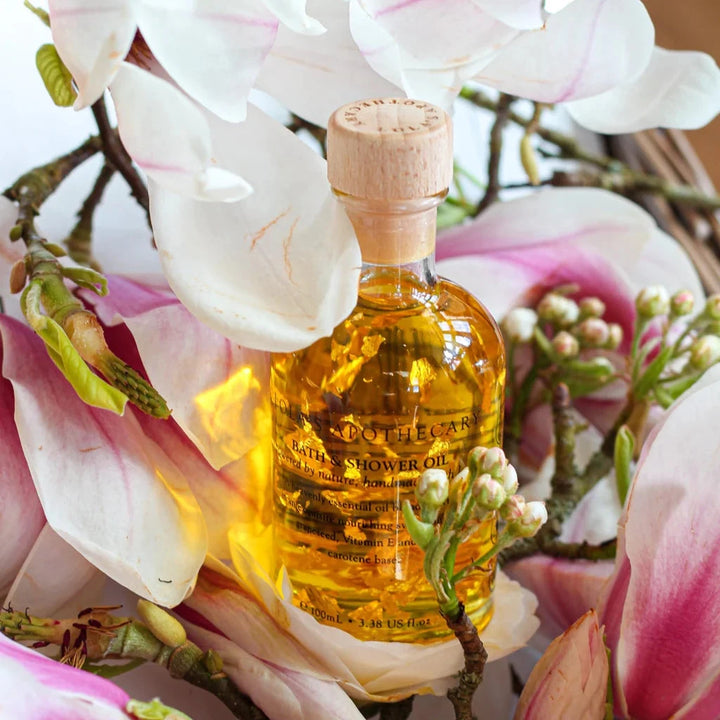 Eine Glasflasche Bath & Shower Oil von Lola's, steht zwischen Orchideenblüten.