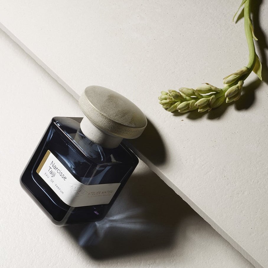 Perfume bottle Narcisse Taiji lying diagonally, next to it a flower North Glow