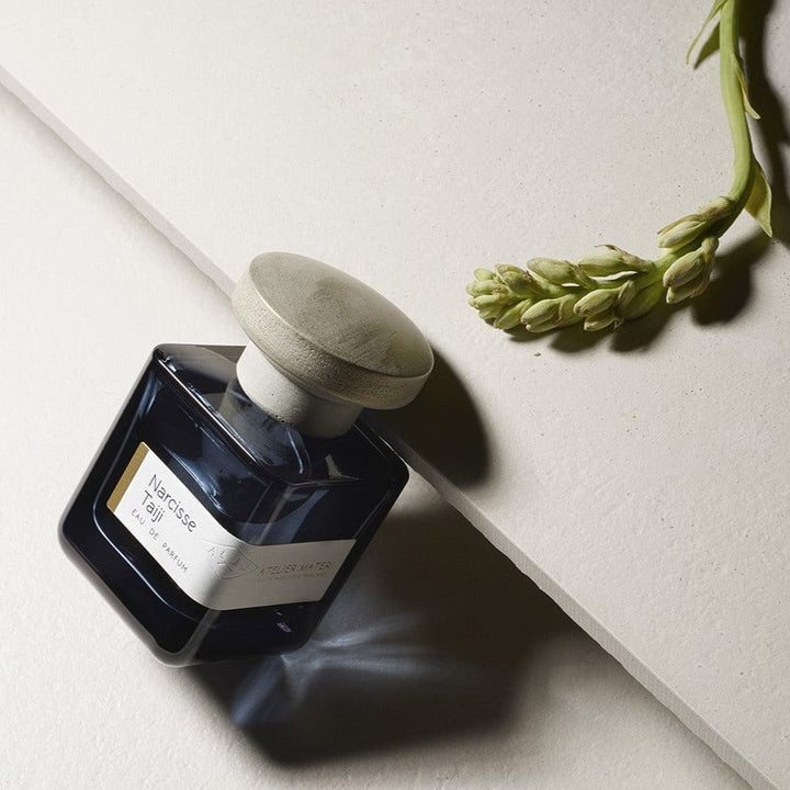 Perfume bottle Narcisse Taiji lying diagonally, next to it a flower