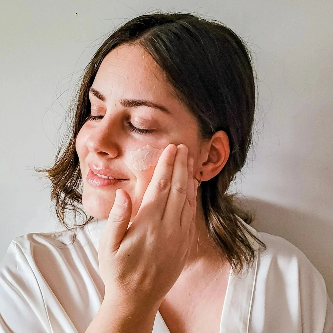 A woman applies a cream to her face and strokes her cheek with one hand. North Glow