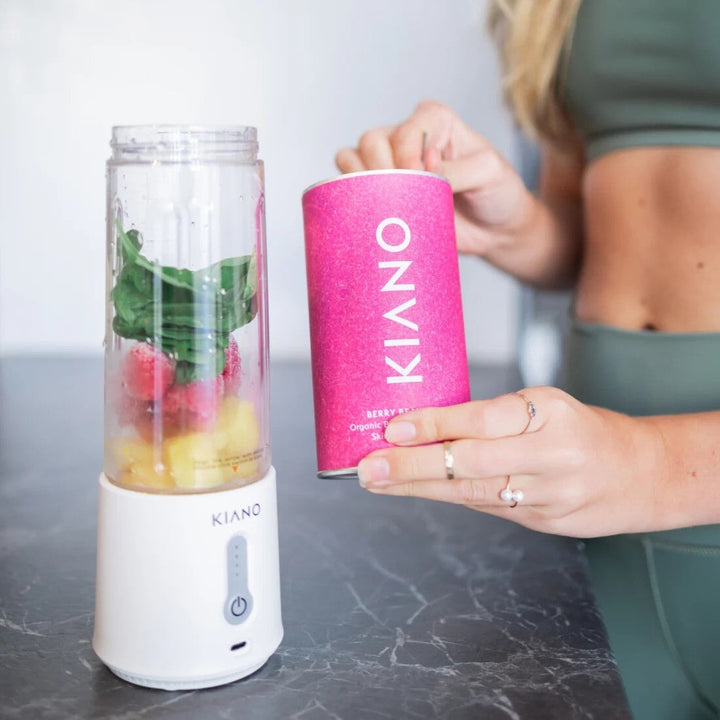 Kiano Portable Blender stands open on a table, filled with berries, fruit and leafy vegetables.