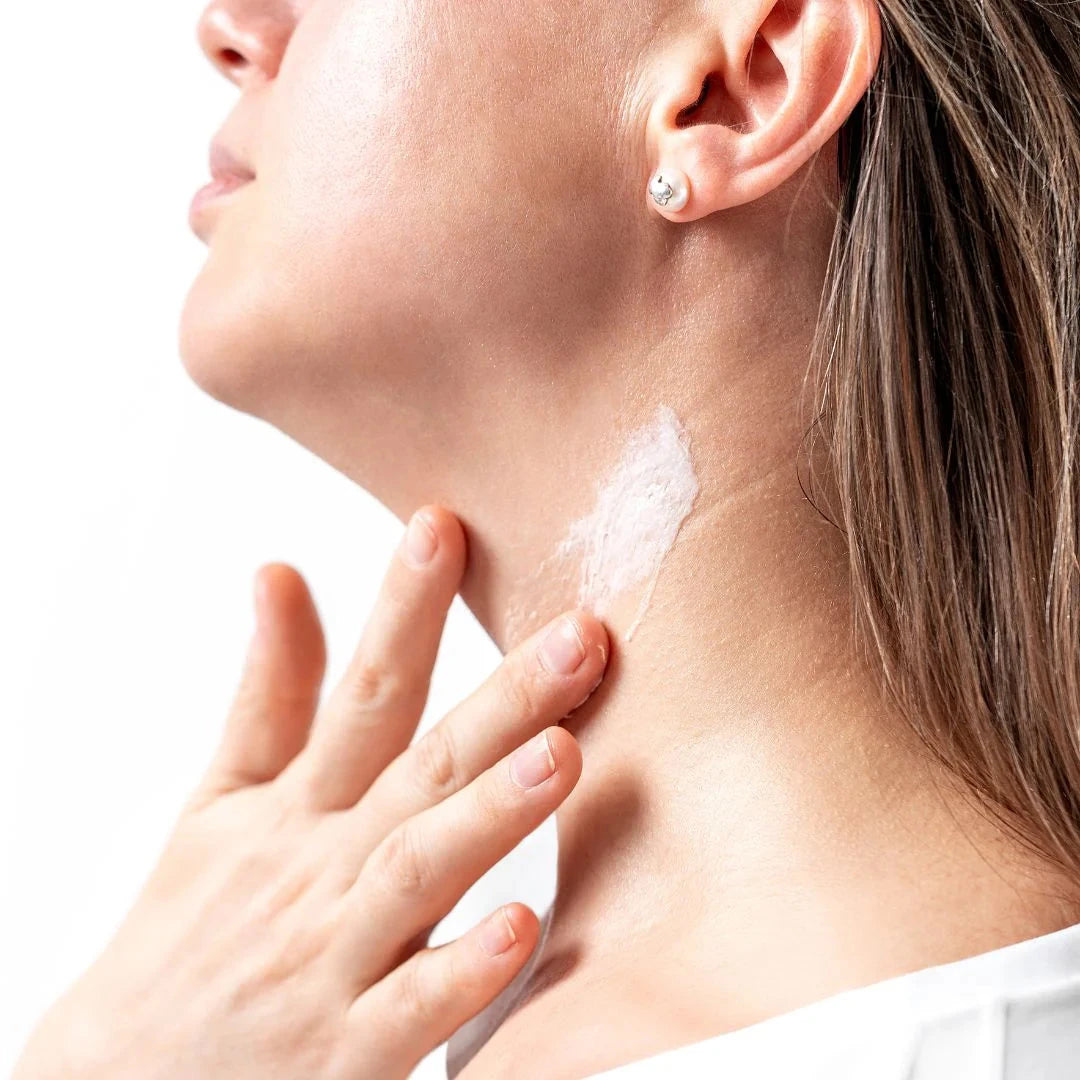 A woman applies cream to her neck with one hand. North Glow