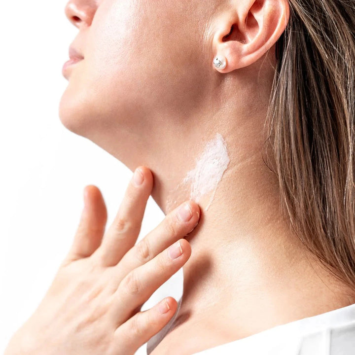 A woman applies cream to her neck with one hand.