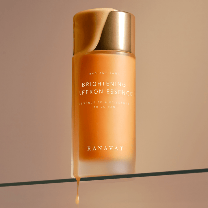 Von der Schraubglasflasche Radiant Rani Brightening Saffron Essence mit goldenem Deckel tropft Inhalt herunter.