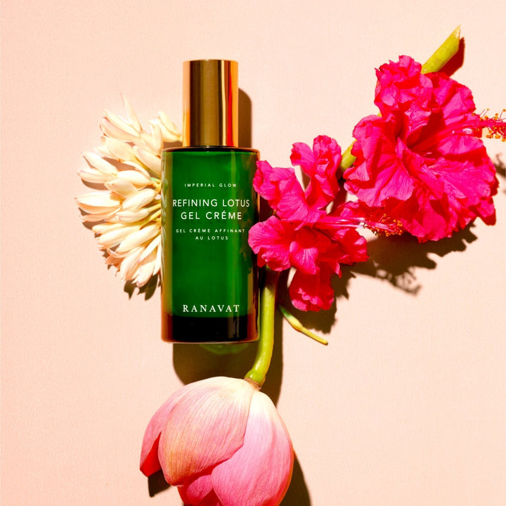Green glass bottle with golden lid Ranavat Refining Lotus Gel Crème against a cream-colored background decorated with various flowers.