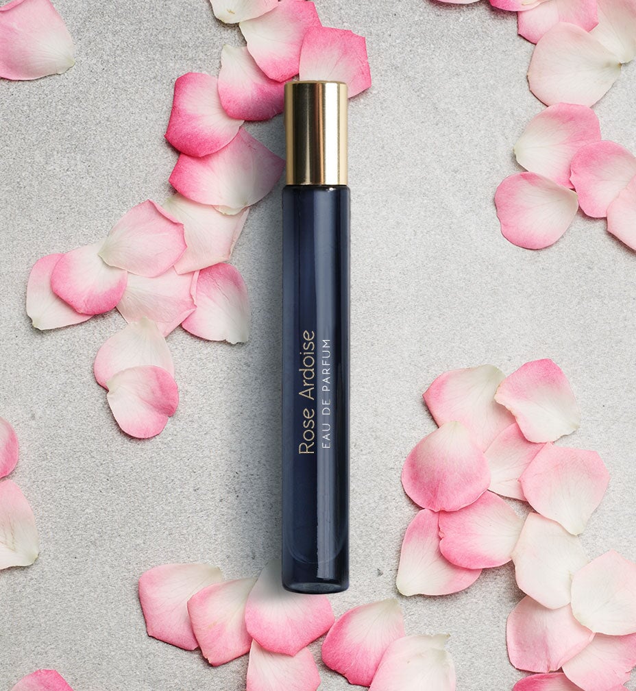 Dark blue, narrow glass jar with golden lid "Rose Ardoise" by Atelier Materi surrounded by roses. North Glow