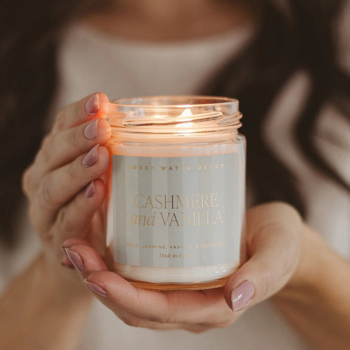 2 Hände halten eine brennende Sojawachskerze Cashmere and Vanilla.