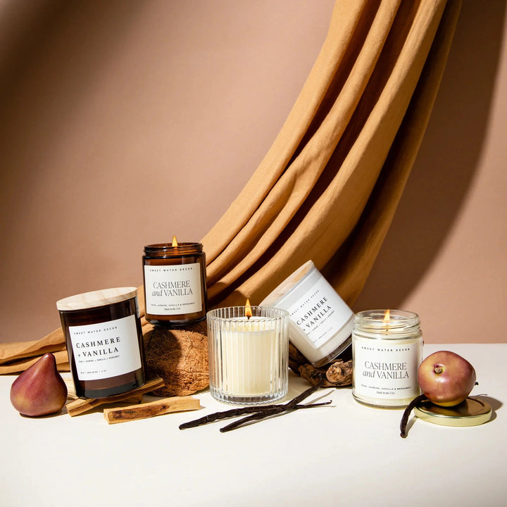 Verschiedene Gläser der Sojawachskerze Cashmere and Vanilla stehen zwischen Vanilleschoten und Birnen.