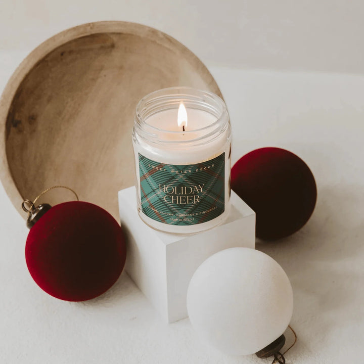 HOLIDAY CHEER" candle surrounded by Christmas baubles and a wooden bowl.