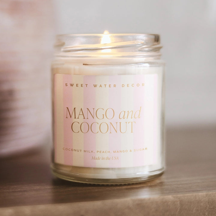 Brennende Sojawachskerze Mango and Coconut steht auf einer hölzernen Unterlage.
