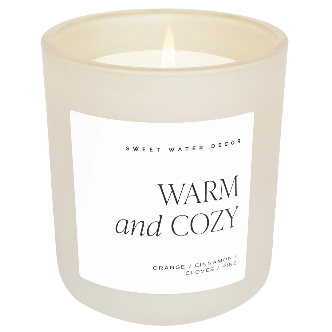 Cremefarbenes Milchglas mit Kerze der Aufschrift WARM and COZY. North Glow