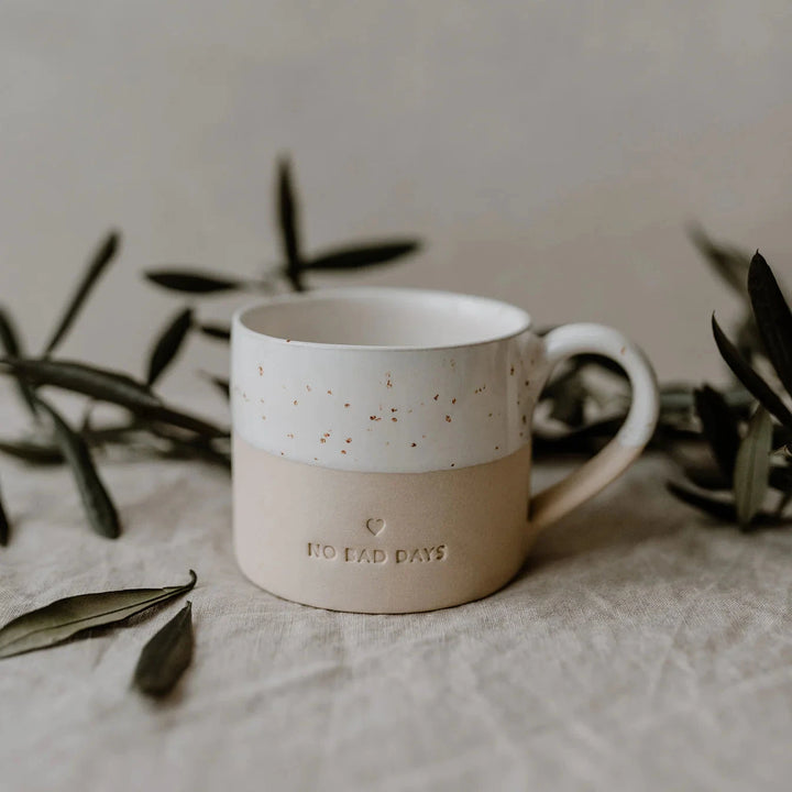 Mug embossed with "no bad days" by Eulenschnitt on linen cloth, surrounded by dark green leaves.