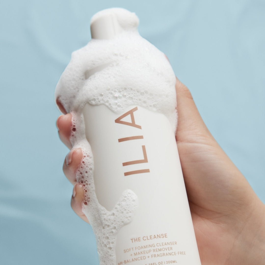 Eine Hand hält eine  ILIA The Cleanse Pumpflasche an der Schaum herunterläuft. North Glow