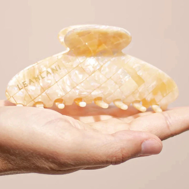 Mother-of-pearl-colored hair clip from LEAHLANI lies on the palm of one hand.