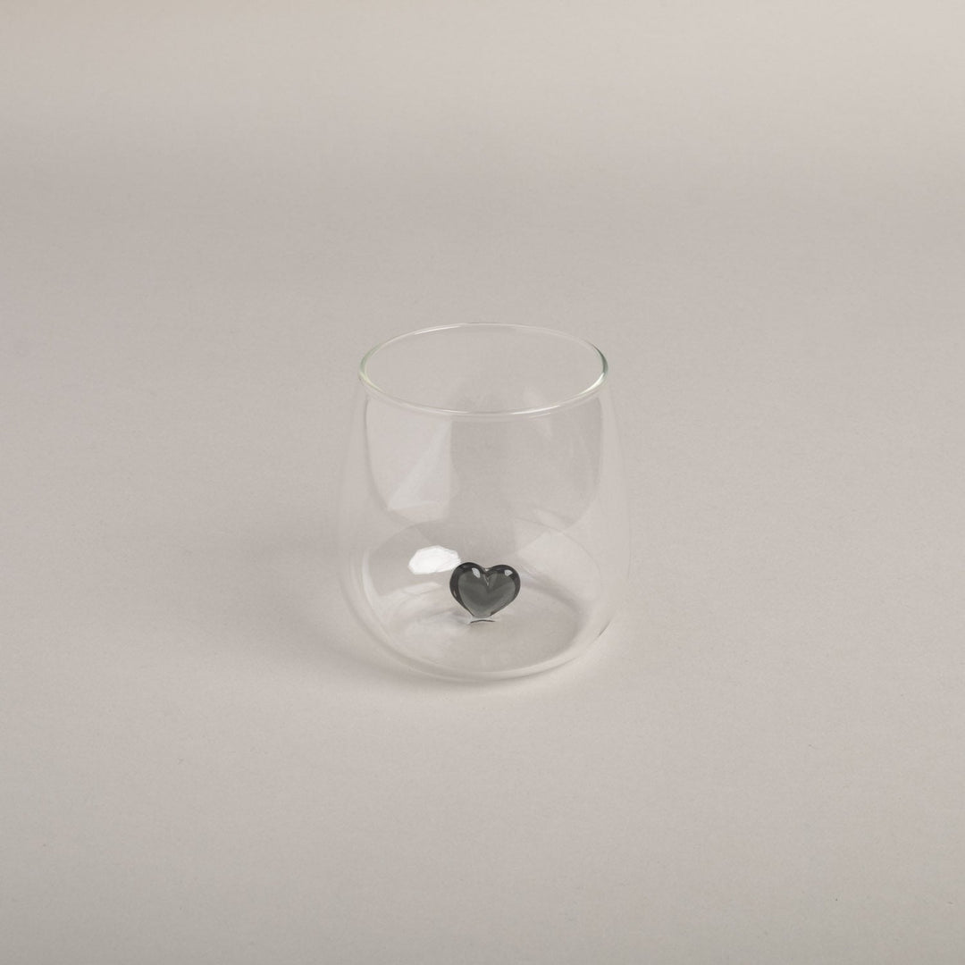 Bellied drinking glass with black heart in the center of owl cut stands against a light background. North Glow