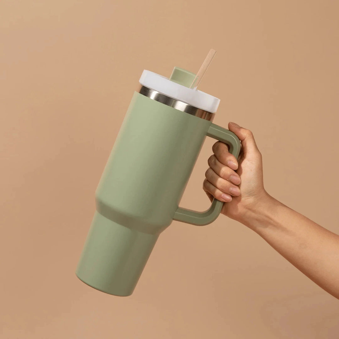 Eine Hand hält einen grünen Tumbler / Thermobecher von Sweet Water Decor vor hellem Hintergrund. North Glow