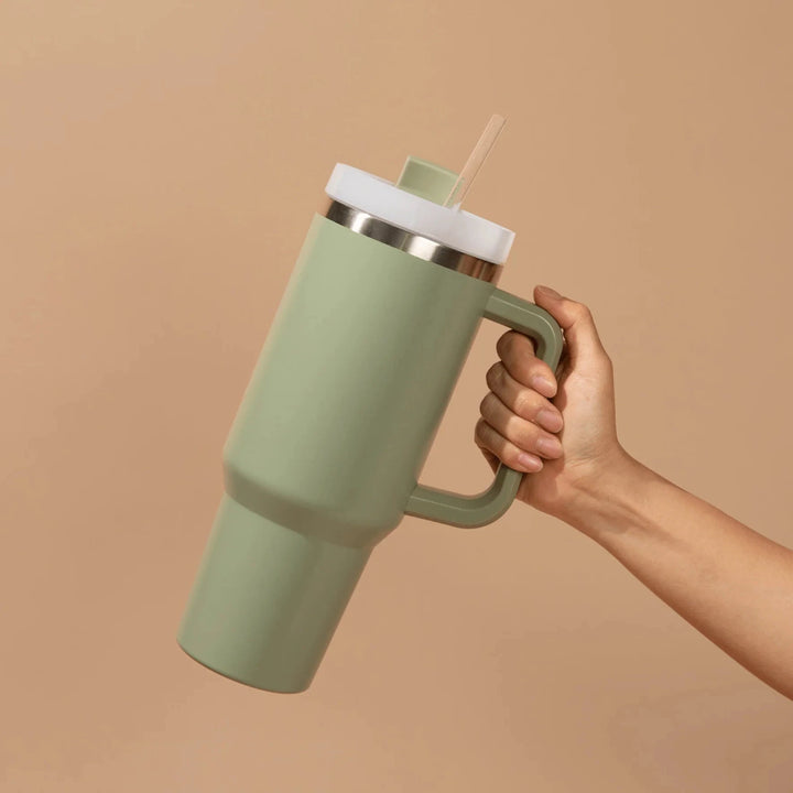 Eine Hand hält einen grünen Tumbler / Thermobecher von Sweet Water Decor vor hellem Hintergrund.