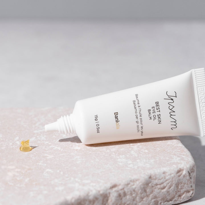 Open Ipsum Best Skin Eye Oil Balm tube lies on a stone slab with a blob of product in front of it.