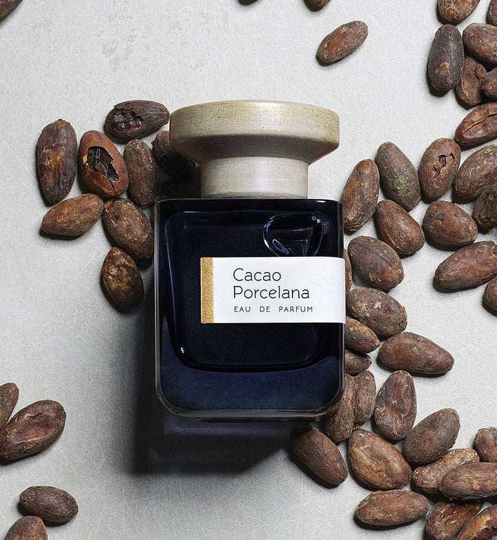 Dark blue glass bottle with gray lid "Cacao Porcelana" by Atelier Materi surrounded by cocoa beans.