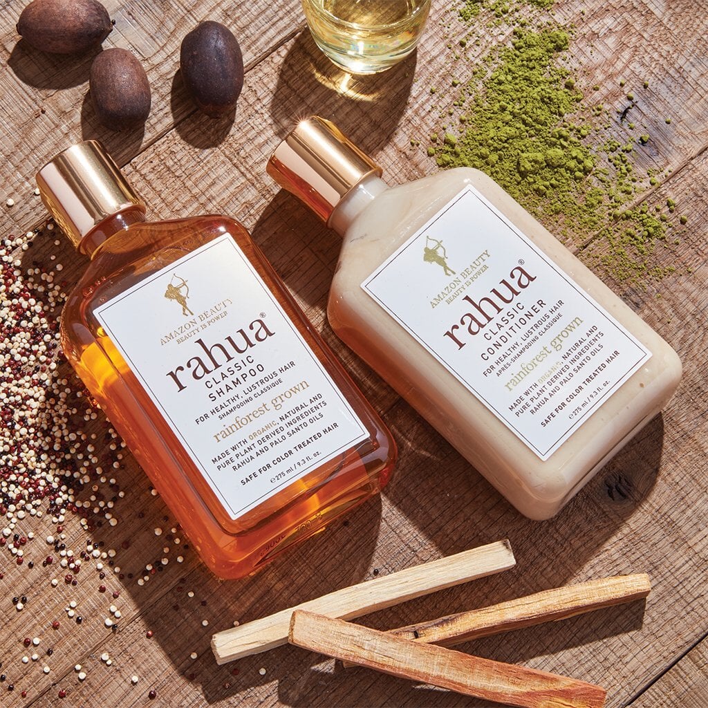 Rahua Classic shampoo and conditioner bottles lie on a table decorated with Palo Santo quinoa, Rahua nut and mathcha powder. North Glow