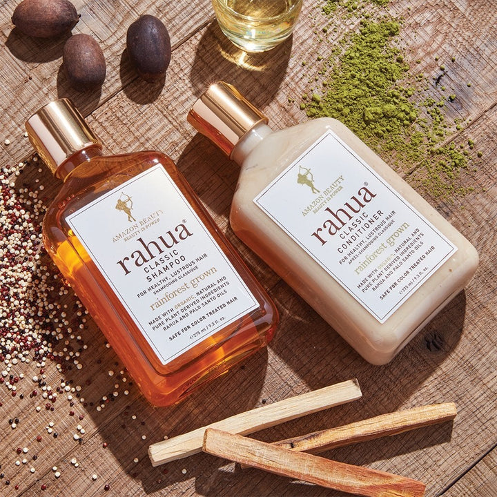 Rahua Classic shampoo and conditioner bottles lie on a table decorated with Palo Santo quinoa, Rahua nut and mathcha powder.