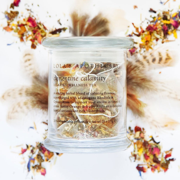 Lola's Apothecary Clementine Calamity Wellness Tea Glass with Tea Bags in Background Rose Petals and Feathers