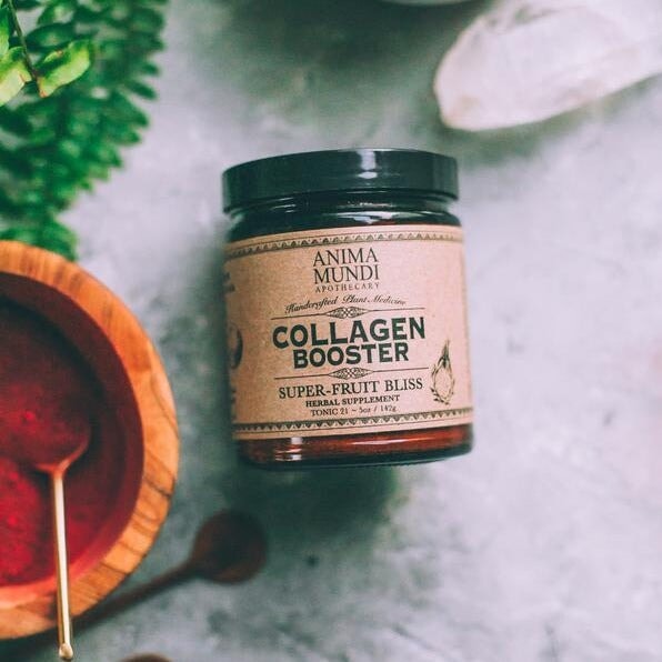 Anima Mundi Schraubglas Collagen Boosgter aus der Vogelperspektive neben einem Mörser gefüllt mit rotem Pulver.