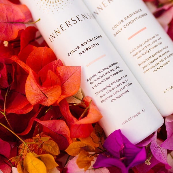Close-up Innersense Color Awakening Hairbath and Color Radiance Daily Conditioner bottles on colorful petals.