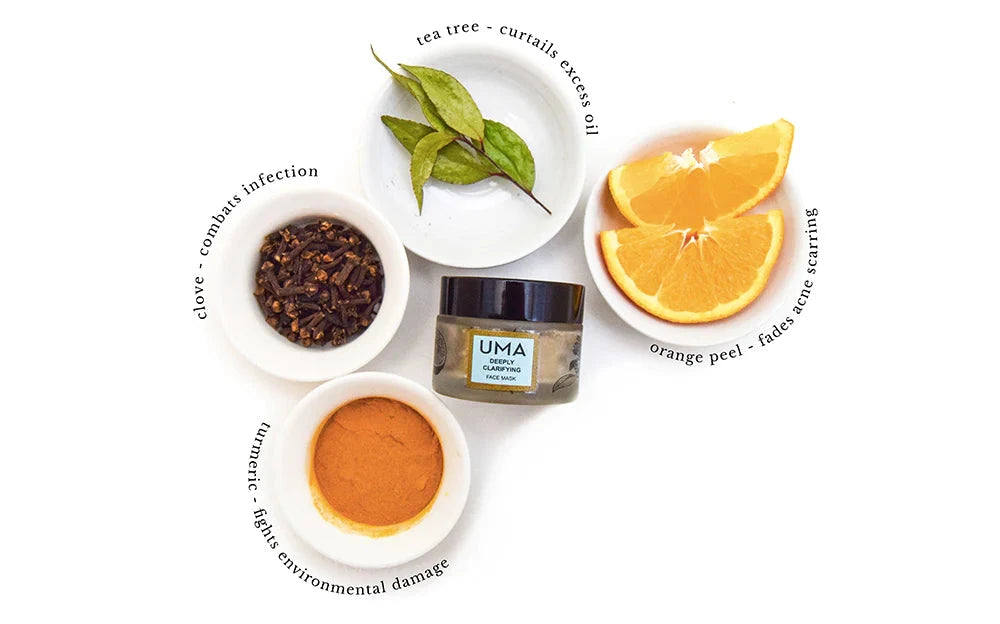 Screw-top jar of UMA Deeply Clarifying Face Mask surrounded by bowls containing cloves, tea tree leaves, orange slices and turmeric powder. North Glow