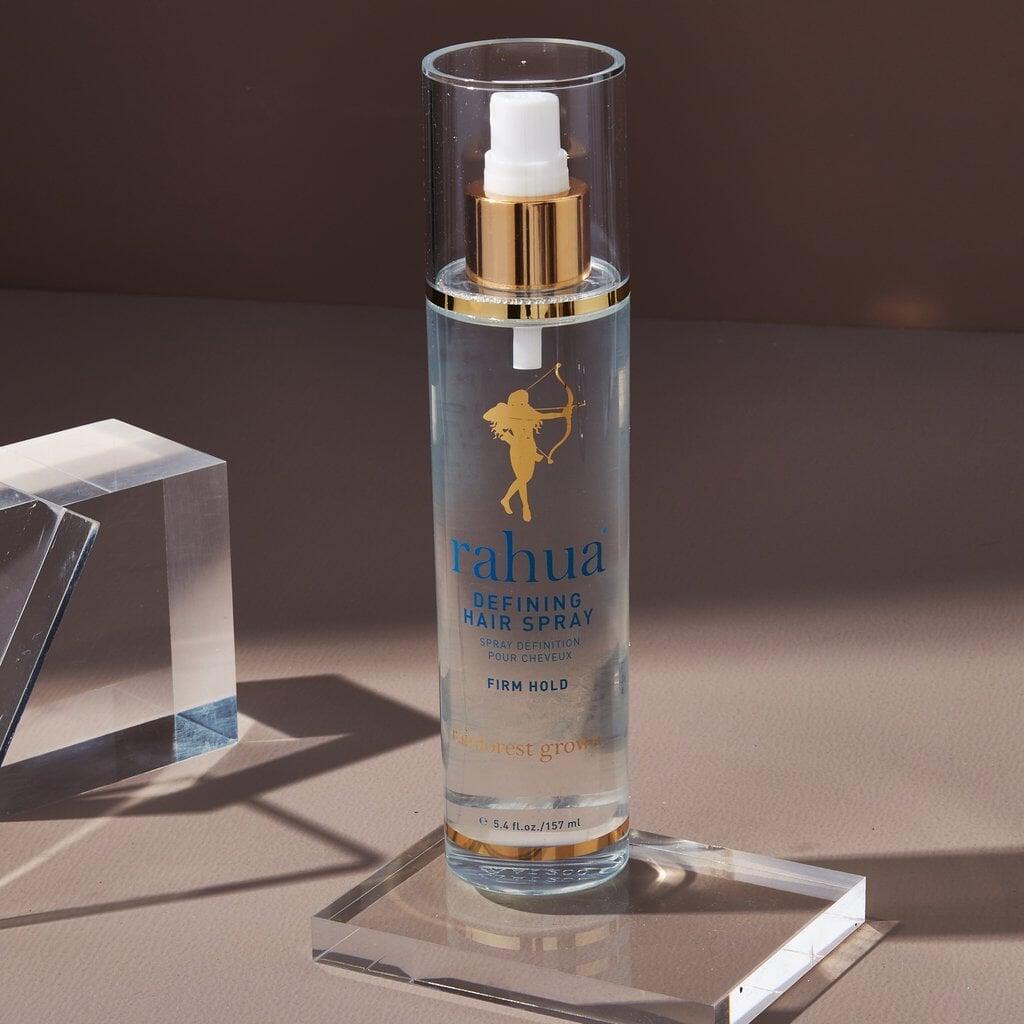 Rahua Defining Hair Spray bottle stands on a plexiglass panel against a brown background. North Glow