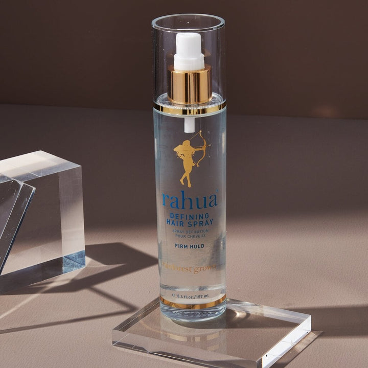 Rahua Defining Hair Spray bottle stands on a plexiglass panel against a brown background.