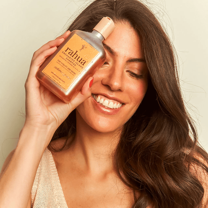 Laughing woman holds Rahua Enchanted Island bottle in her hand in front of her face.