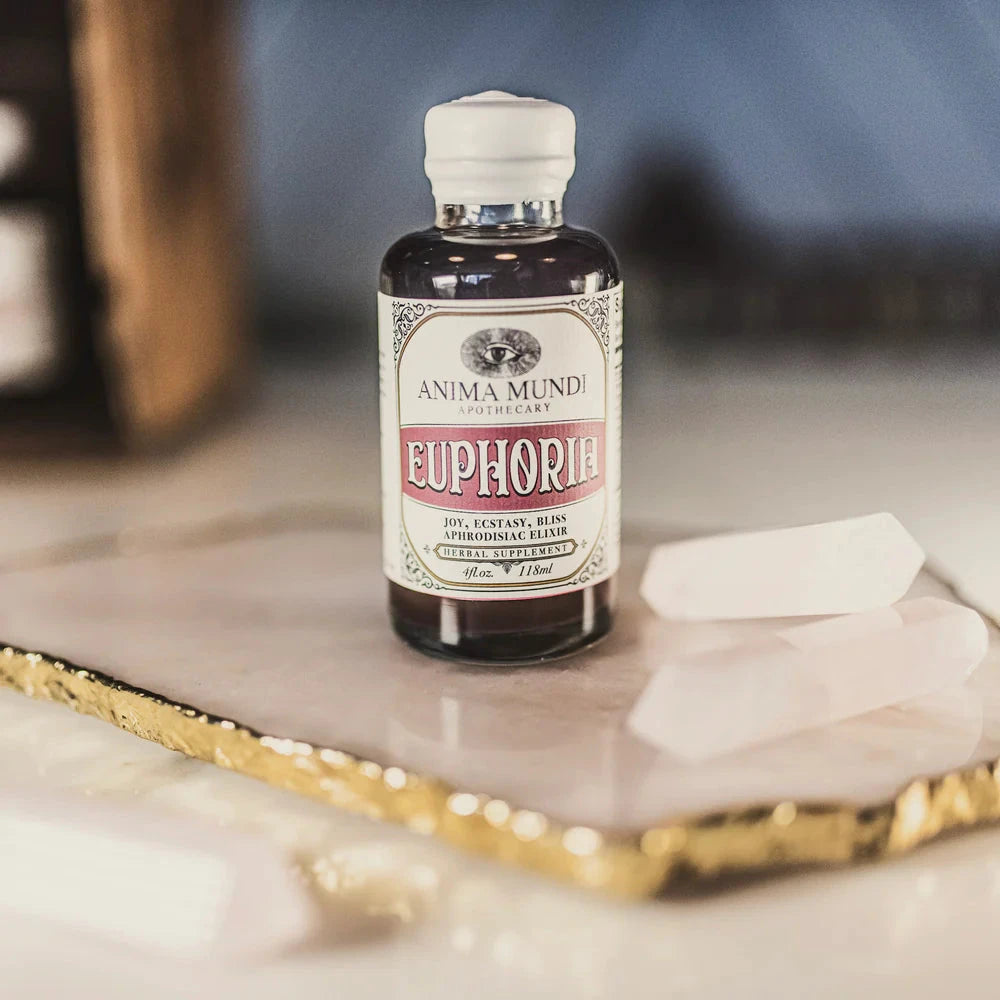 Anima Mundi Glasflasche Euphoria steht auf einer goldumrandeten Platte, daneben 2 Edelsteine.