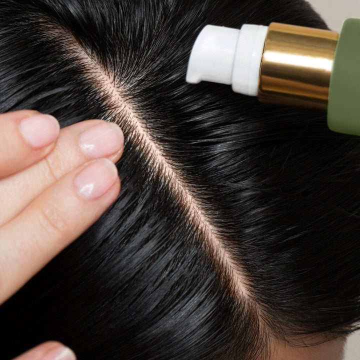 Close-up of a scalp, dark hair parted and bottle top of the Founder`s Blend Scalp & Hair Treatment bottle.