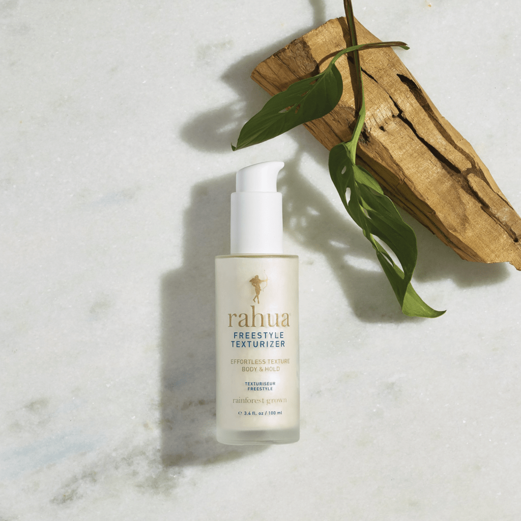Rahua Freestyle Texturizer bottle against a cream background, decorated with palm leaves and logs. North Glow