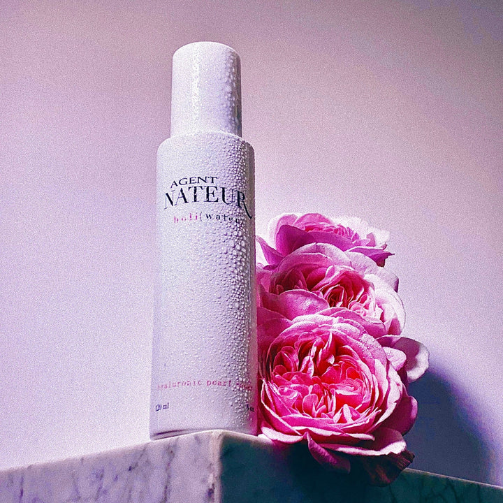 Holi (Water) pearl and rose Essence white bottle with pink roses on white marble table