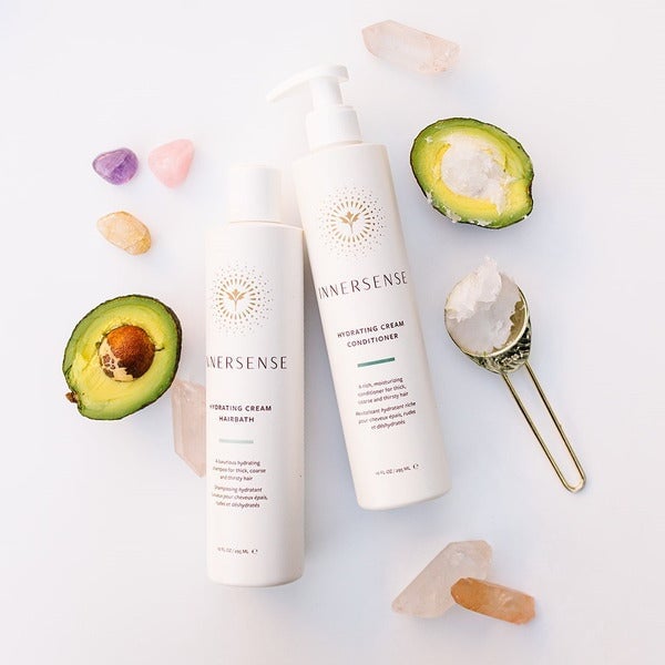 Innersense Hydrating Cream Hairbath and Conditioner bottles lying on white background next to 2 avocado halves, one filled with ice cream.