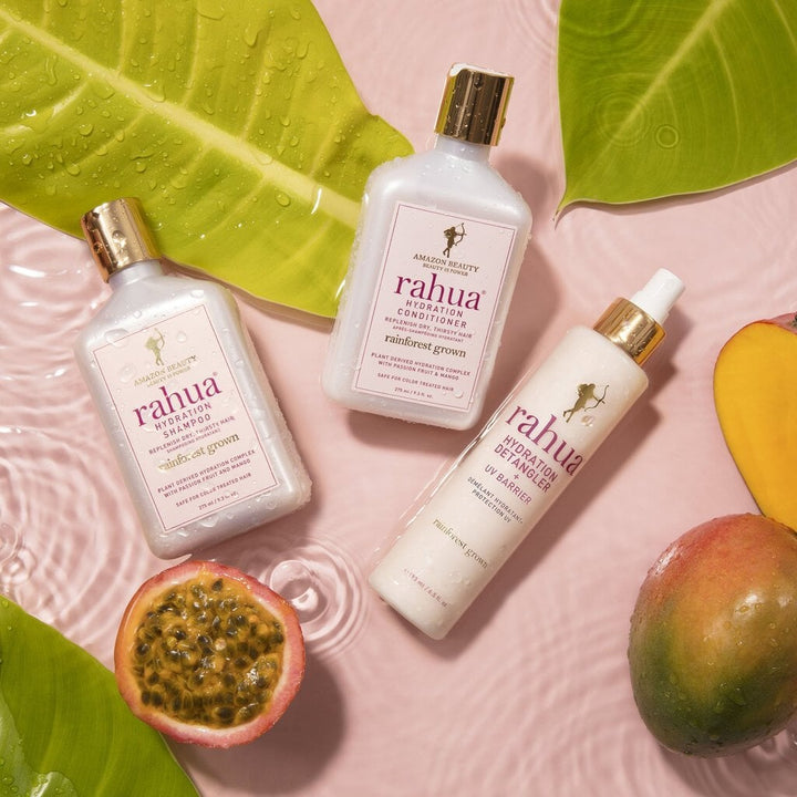 Rahua Hydration series, 3 bottles lying in water decorated with passion fruit, mango and palm leaves.