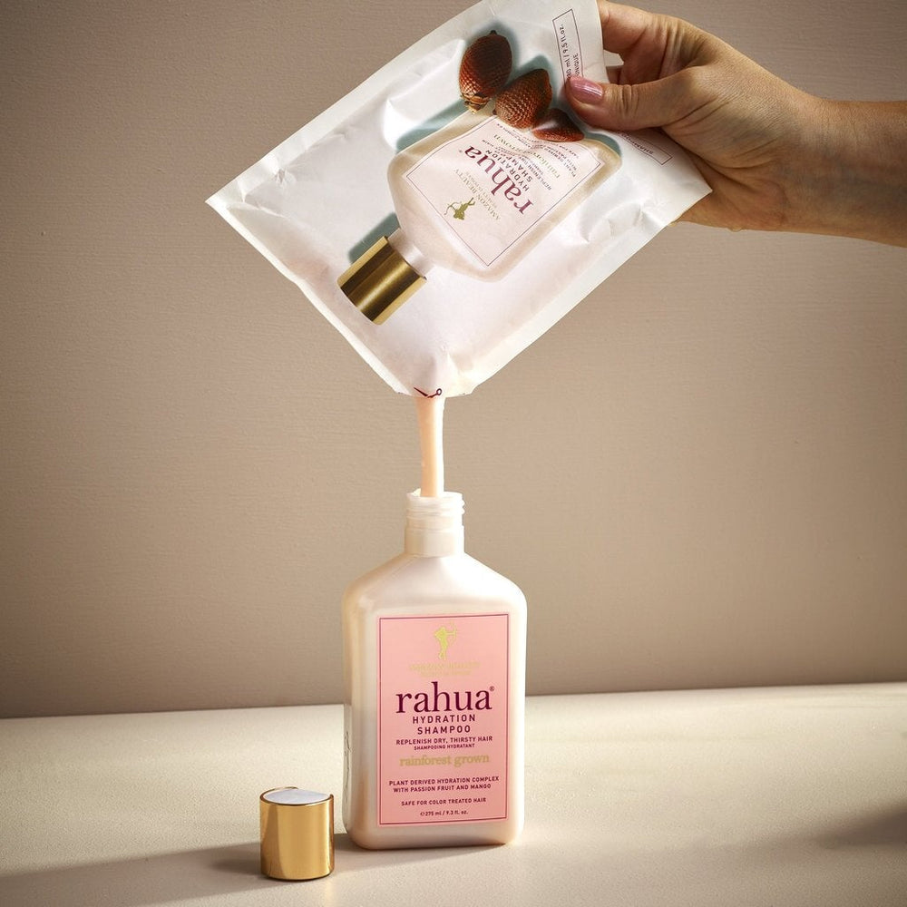 Hand holds Rahua Hydration Shampoo Refillpouch and pours the contents into the bottle.