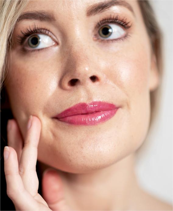 Close-up of a woman's face, made up with Ere Perez Mango Lip Honey lip gloss in Crush. North Glow