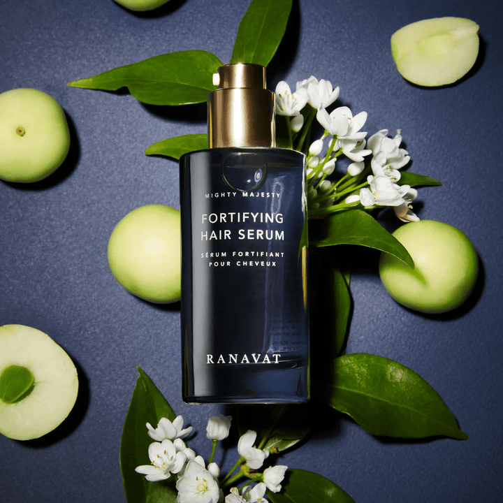 Ranavat Mighty Majesty hair serum on blue background with leaves, white flowers and green apples