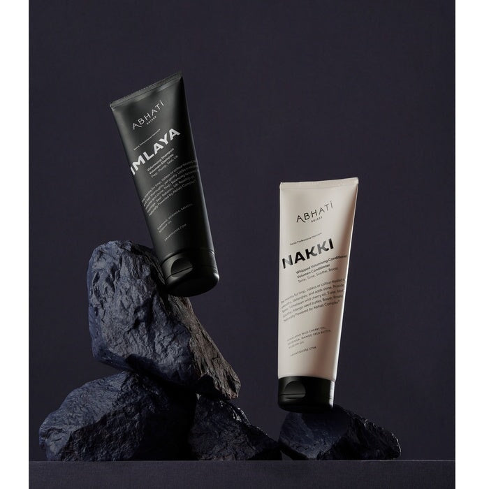 Abhati Suisse Nakki Conditioner und Imlaya Shampoo Tuben stehen auf schwarzen Steinen. North Glow