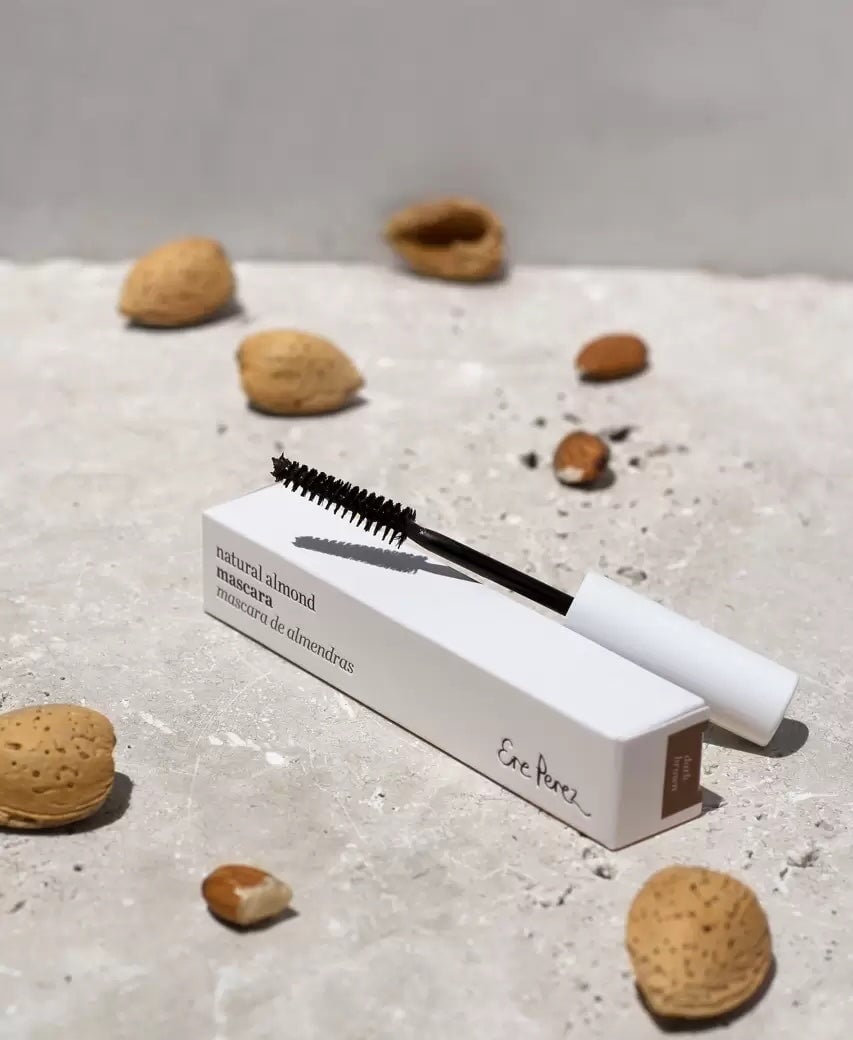 The eyelash brush and packaging of the Ere Perez Natural Almond Mascara lie between almonds. North Glow