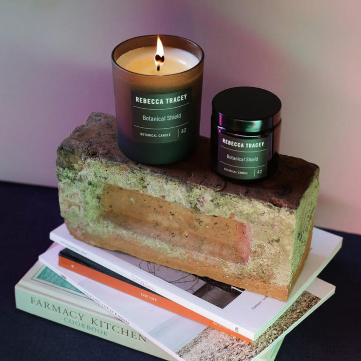 Two candles by Rebecca Tracey on a stone, with books and magazines underneath.