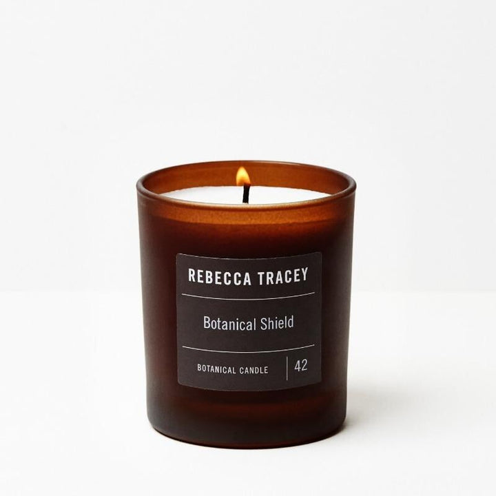 Burning candle "Botanical Shiel" by Rebecca Tracey against a white background.