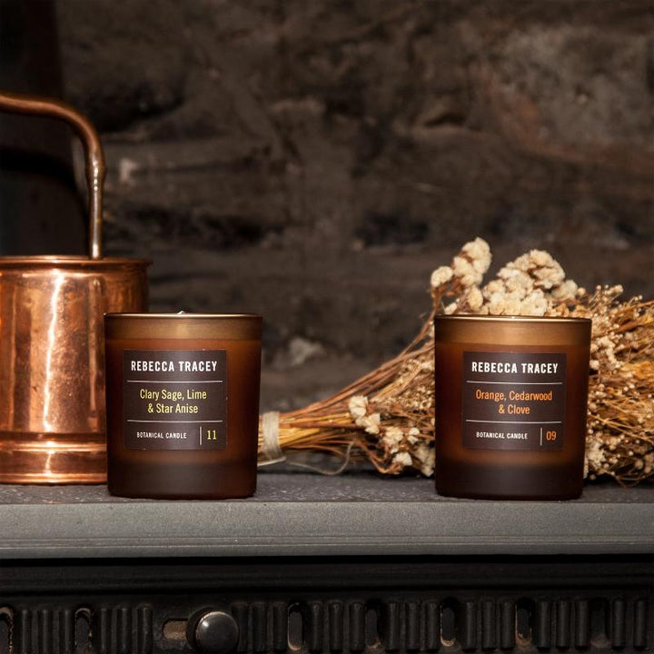 Two candle jars by Rebecca Tracey, surrounded by a dried bouquet of flowers and a copper-colored container.