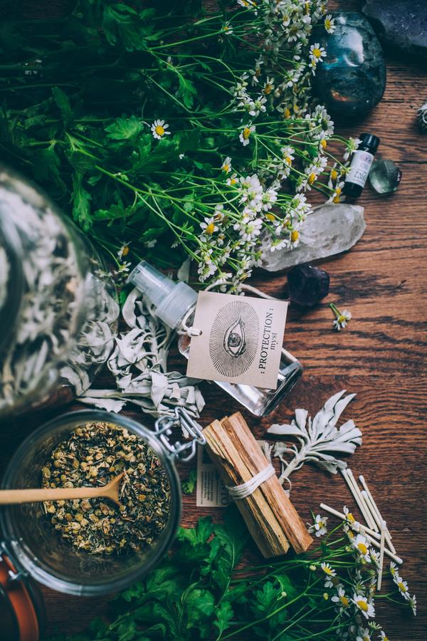 Anima Mundi Palo Santo Glasflasche mit einem großen Papierschild auf dem ein großes Auge abgebildet ist liegt auf verschiedenen Kräutern und Palo Santo Holzbündel. 